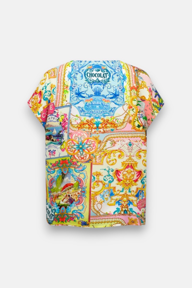 Ein leuchtendes, kurzärmeliges Blusenshirt von Princess Goes Hollywood mit einem Dolce Vita-Aufdruck - mit verschnörkelten Golddetails, Blumen, Pastellfarben, Retro-Werbung und Rahmen - ziert den weißen Hintergrund für einen Vintage-inspirierten Stil.