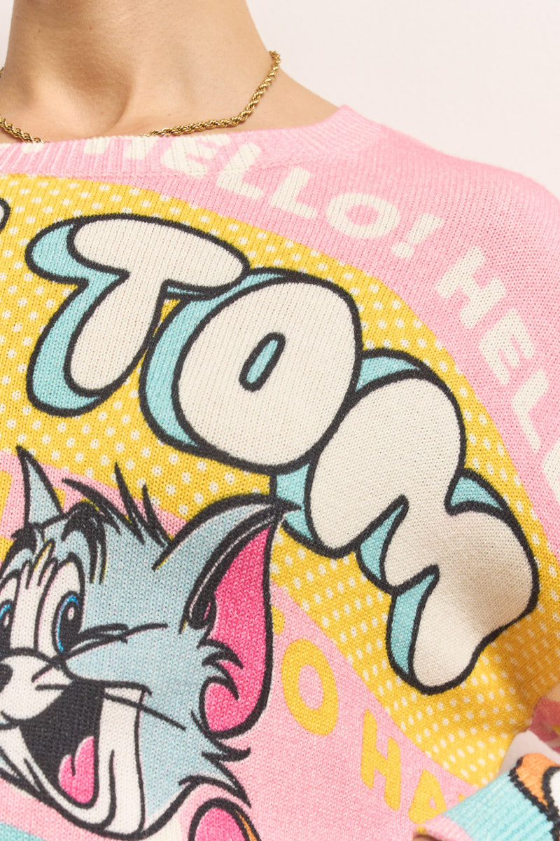 Nahaufnahme eines rosa Princess Goes Hollywood Tom &amp; Jerry-Pullovers mit einem bunten Cartoon-Tom, der zwinkert. Darüber ist fett "Tom" in gelben, weißen und blauen Details aufgedruckt. Die Trägerin trägt außerdem eine goldene Halskette.