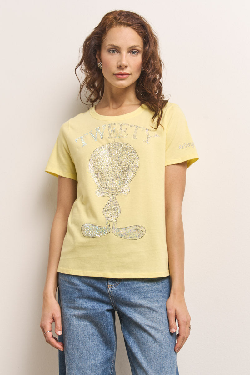 Eine Frau mit gewelltem, rötlich-braunem Haar trägt ein Princess Goes Hollywood Tweety T-Shirt aus Baumwolle, auf dem ein glitzernder Tweety Bird und "TWEETY" in silberner Strassdeko abgebildet sind. Sie trägt dazu eine blaue Jeans und steht vor einer hellen Wand.