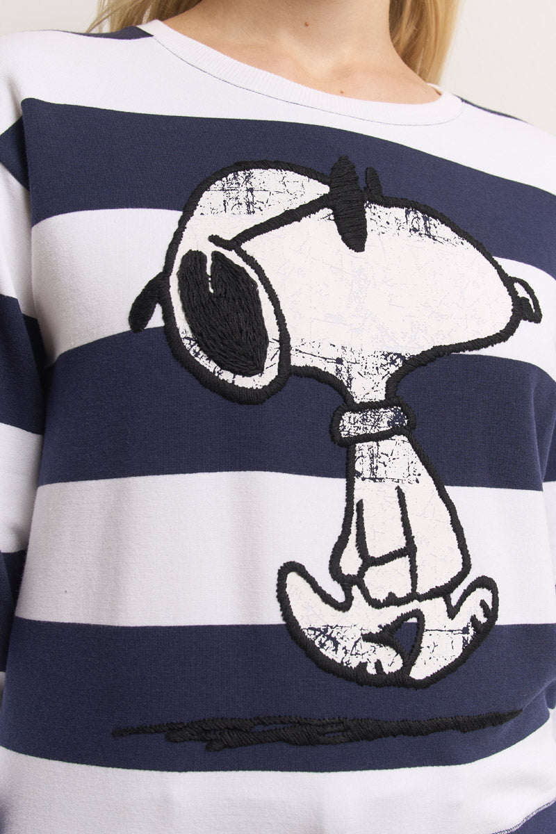 Nahaufnahme einer Person, die ein Princess Goes Hollywood gestreiftes Sweatshirt aus Baumwollmix mit breiten marineblauen und weißen Streifen trägt, auf dem ein großer gestickter Snoopy-Aufdruck zu sehen ist, der den Peanuts-Hund mit gesenktem Kopf zeigt.