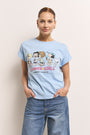 Eine Frau mit braunen Haaren in einem Pferdeschwanz trägt goldene Ohrringe, blaue Jeans und ein hellblaues Princess Goes Hollywood Baumwolle T-Shirt mit einem Peanuts-Aufdruck und dem Text "SUMMER GIRLS PRINCESS * PEANUTS". Sie steht vor einem hellen Hintergrund, die Hände in den Taschen.