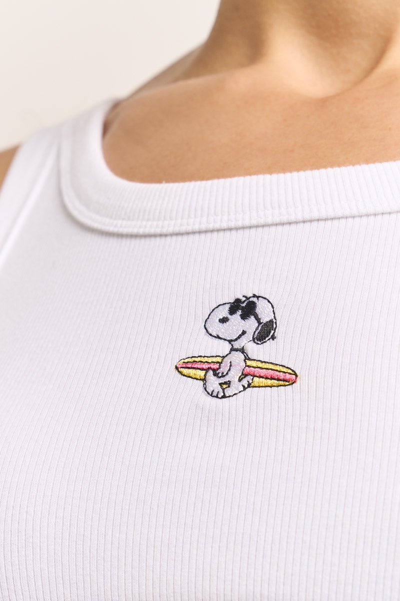 Nahaufnahme eines weißen, gerippten Baumwoll-Tanktops von Princess Goes Hollywood mit Snoopy-Stickerei, der ein gelb-rot gestreiftes Surfbrett auf der Brust hält. Sichtbar sind Halsausschnitt und obere Brust; das Gesicht ist nicht im Bild.