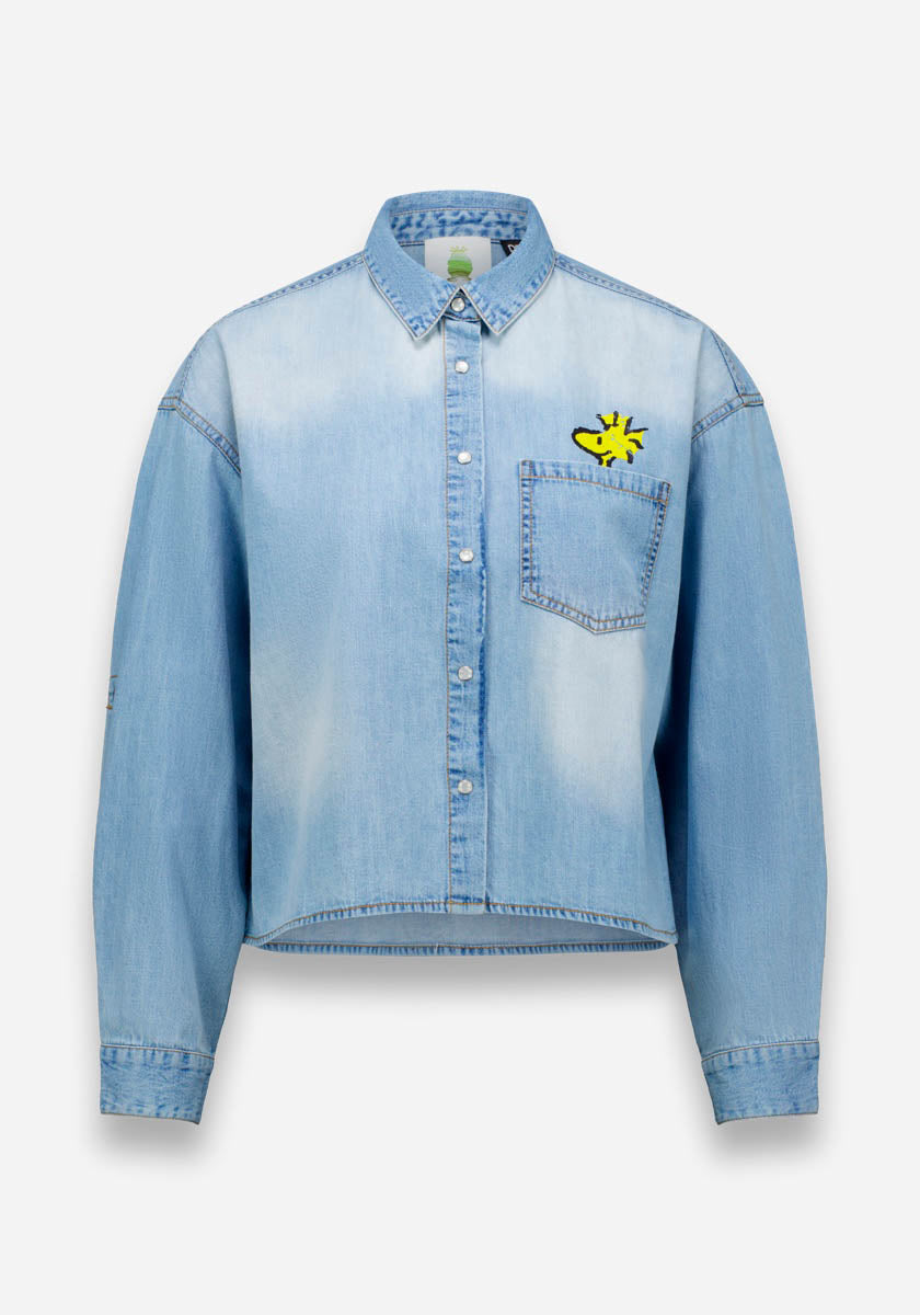 Hellblaues Princess Goes Hollywood Jeanshemd mit langen Ärmeln und geknöpfter Front, aus Baumwolle. Es hat eine Brusttasche mit einer kleinen gelben Sonnengrafik darüber und einen leicht verblichenen Vintage-Look.