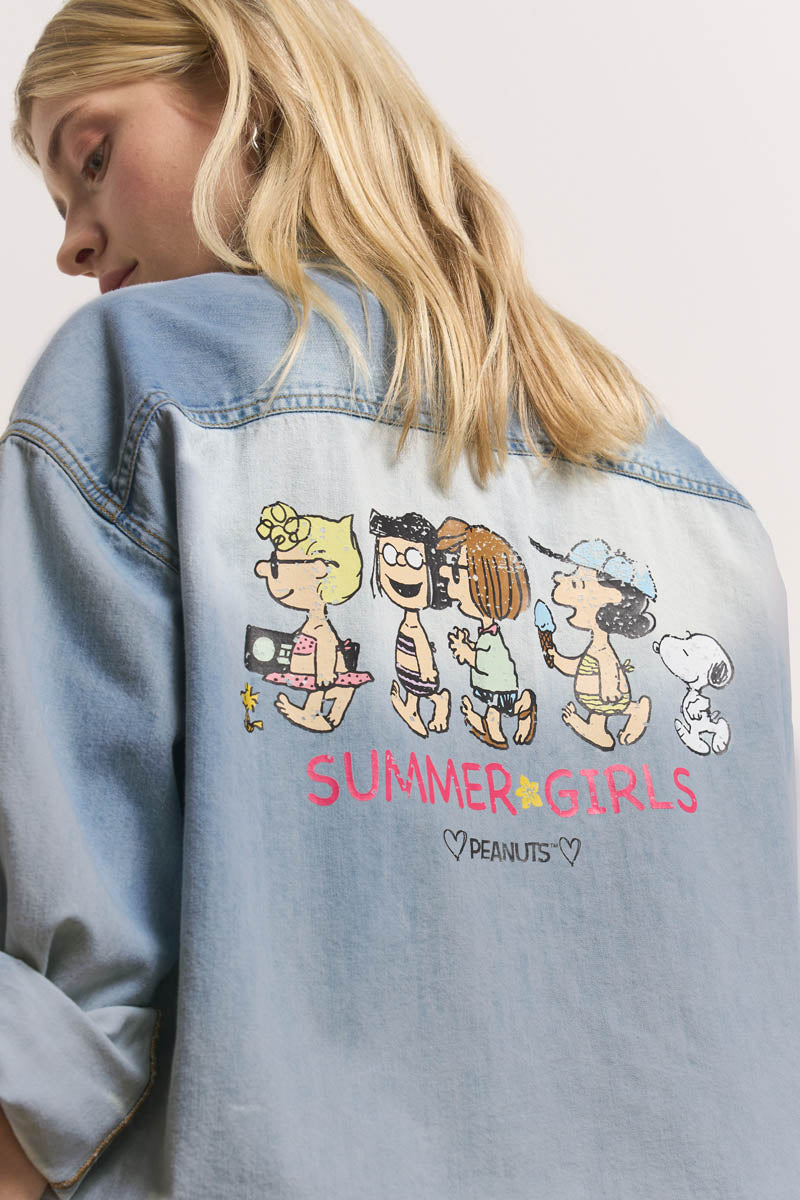 Eine Frau mit langen blonden Haaren trägt ein leichtes Baumwoll-Jeanshemd von Princess Goes Hollywood mit einem farbenfrohen Peanuts-Sommermotiv mit Lucy, Patty, Marcie und Snoopy und dem fetten rosa Schriftzug "SUMMER GIRLS ♥ PEANUTS ♥" darunter.