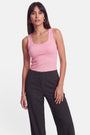 Eine Frau mit glattem, dunklem Haar trägt ein rosa Basic-Top mit Rundhalsausschnitt und eine schwarze Nadelstreifenhose mit hoher Taille. Sie steht vor einem schlichten weißen Hintergrund, blickt nach vorne, einen Arm entspannt an der Seite, die andere Hand leicht auf dem Oberschenkel ruhend.