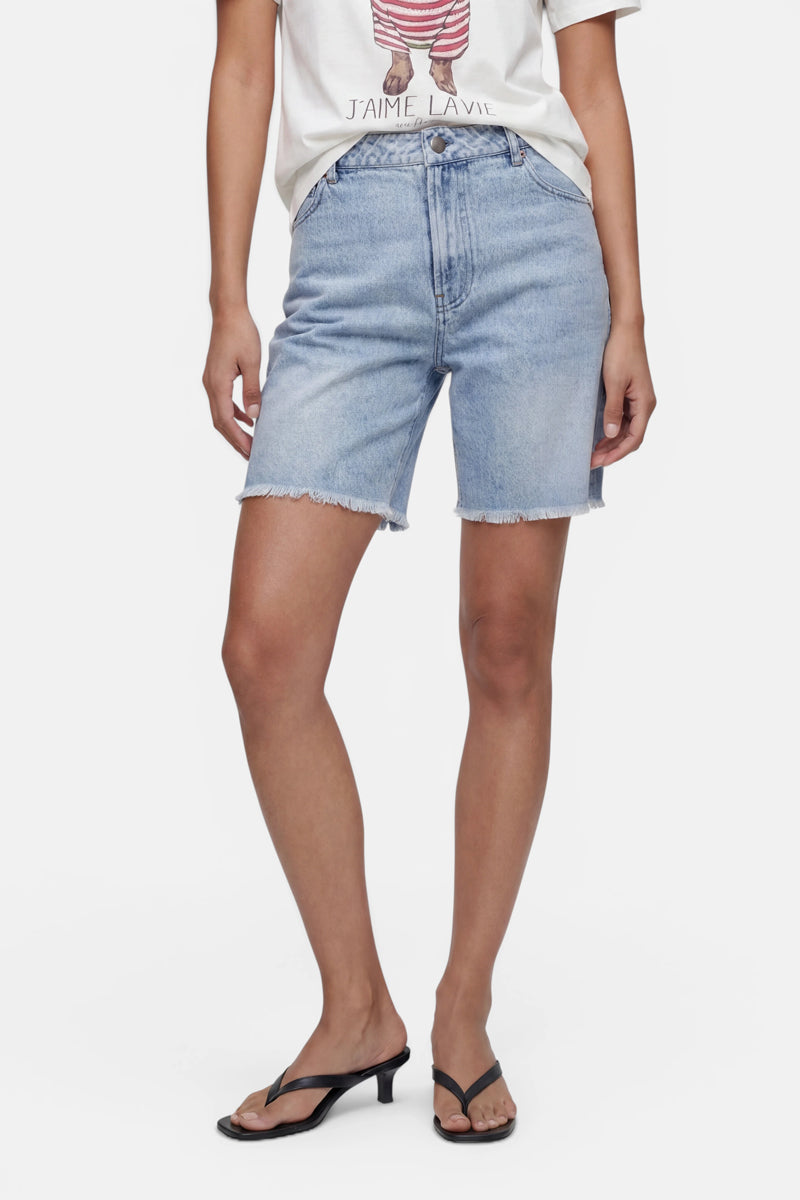 Eine Person ist nur von der Hüfte abwärts zu sehen. Sie trägt hellblaue Jeansshorts von „Princess Goes Hollywood“ mit ausgefranstem Saum, ein weißes T-Shirt mit Aufdruck, das in die Hose gesteckt ist, schwarze Sandalen mit Absatz sowie schwarze Flip-Flop-Riemen vor einem weißen Hintergrund.