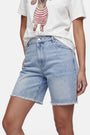 Eine Person trägt Jeansshorts der Marke „Princess Goes Hollywood“ mit ausgefranstem Saum in heller Waschung und ein weißes T-Shirt mit Dackel-Aufdruck im Streifen-Look; die Aufnahme zeigt die Person von den Schultern bis zu den Oberschenkeln vor einem neutralen Hintergrund.