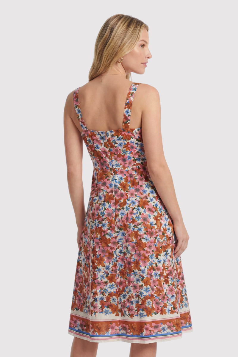 Eine hellhäutige Frau mit glattem blondem Haar trägt ein ärmelloses Seiden-Mididress von Princess Goes Hollywood in limitierter Auflage mit einem bunten Blumenmuster in Rosa, Orange, Blau und Weiß. Sie steht abgewandt und blickt zur Seite.