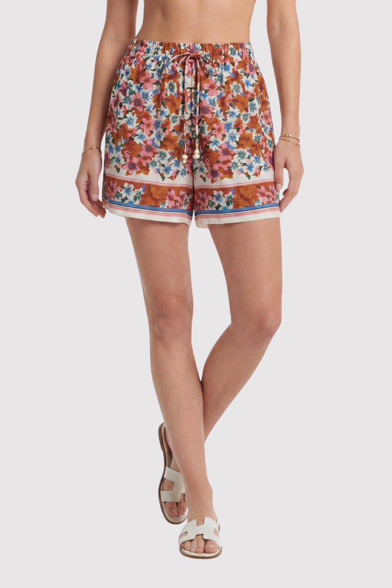 Eine Person trägt Princess Goes Hollywood Blumenprint Seidenshorts mit Tunnelzug in der Taille und breiten horizontalen Streifen in der Nähe des Saums, gepaart mit einem Goldarmband und weißen Sandalen. Der Hintergrund ist einfarbig und hell. Limitierte Auflage.