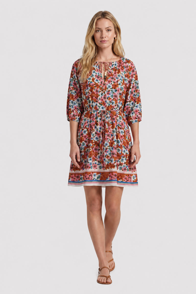 Eine Frau mit langem blondem Haar trägt ein knielanges rotes, geblümtes Kleid mit geraffter Taille, 3/4-Ärmeln und Schlüssellochausschnitt in der Limited Edition von Princess Goes Hollywood. Sie steht mit dem Gesicht nach vorne in braunen flachen Sandalen vor einem schlichten weißen Hintergrund.