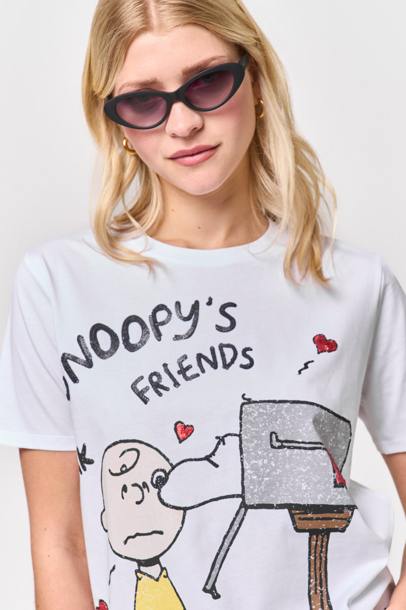 Eine Frau mit langen blonden Haaren trägt eine dunkle Sonnenbrille mit Katzenaugen und ein weißes Princess Goes Hollywood Snoopy T-Shirt aus Baumwolle, auf dem ein verblasster Aufdruck von Snoopy, der Charlie Brown küsst, inmitten roter Herzen und dem Text "SNOOPYS FRIENDS" zu sehen ist.