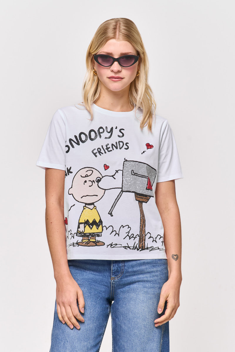 Eine blonde Frau mit Sonnenbrille trägt ein Princess Goes Hollywood T-Shirt aus Baumwolle in limitierter Auflage, auf dem Charlie Brown neben einem Briefkasten mit Herzen und dem Schriftzug "Snoopys Friends" abgebildet ist, gepaart mit einer blauen Jeans vor weißem Hintergrund.