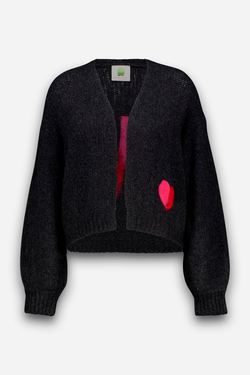 Eine dunkelgraue, langärmelige Strickjacke mit verkürztem Schnitt, gefertigt aus einer luxuriös weichen Merino-Alpaka-Mischung. Sie ist auf einer Seite in Taillenhöhe mit einer kleinen, leuchtend pink-roten Herz-Intarsie verziert und hat keine sichtbaren Knöpfe oder Verschlüsse. Der Ausschnitt ist schlicht V-förmig, und das Strickmaterial wirkt weich und strukturiert.