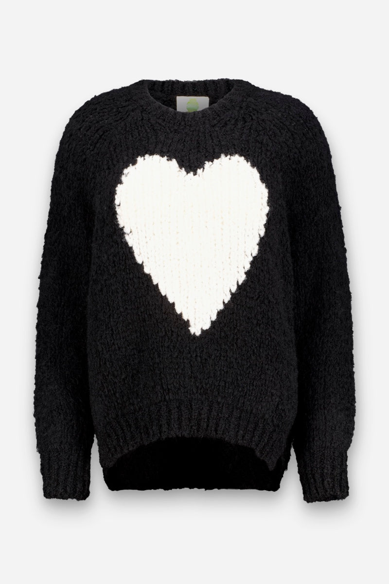 Ein schwarzer, langärmeliger Strickpullover mit einem großen weißen Herzmotiv auf der Brust. Der Pullover hat einen gerippten Rundhalsausschnitt, gerippte Ärmelbündchen und einen gerippten Saum sowie eine leicht lockere und bequeme Passform aus weichem Wollmischgewebe, das sich vor einem schlichten weißen Hintergrund abhebt.