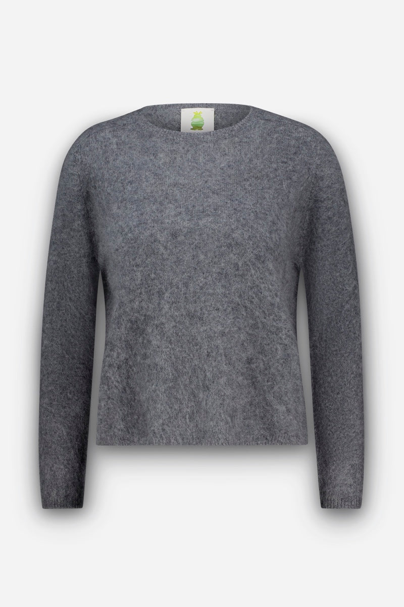Ein grauer Pullover mit langen Ärmeln und Rundhalsausschnitt, der sich durch eine weiche, flauschige Textur aus gebürsteter Wolle auszeichnet. Der Pullover hat eine lockere Passform und weist keine sichtbaren Muster oder Verzierungen auf. Der Hintergrund ist schlicht weiß, und im Halsausschnitt ist ein grünes Etikett zu sehen.