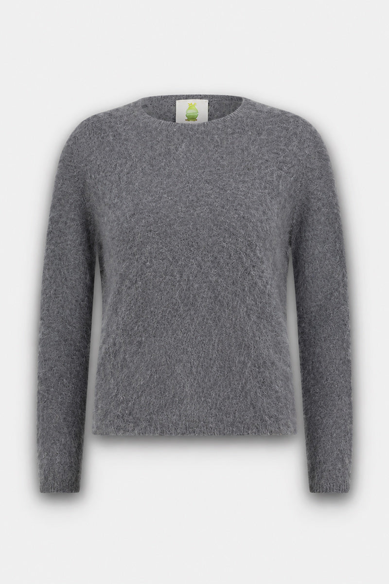Ein weicher, flauschiger, grauer Langarmpullover mit Rundhalsausschnitt wird vor einem schlichten hellgrauen Hintergrund präsentiert. Dieser flauschige Pullover aus gebürsteter Wolle zeichnet sich durch eine schlichte, lockere Passform und ein sichtbares Etikett im Nackenbereich aus, das mit einem grünen Logo verziert ist.