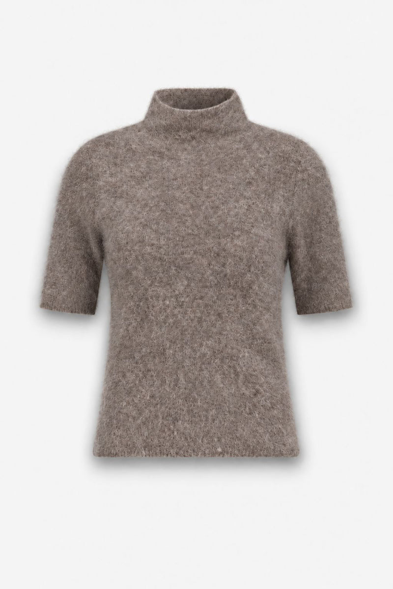 Ein flauschiger, hellbrauner Kurzarmpullover mit lockerem Rollkragen wird vor einem schlichten weißen Hintergrund präsentiert. Der Stoff wirkt weich und leicht flauschig, erinnert an gebürstete Wolle und verleiht dem Pullover ein gemütliches Aussehen. Der Pullover ist schlicht gehalten und hat eine einfache, klassische Silhouette.