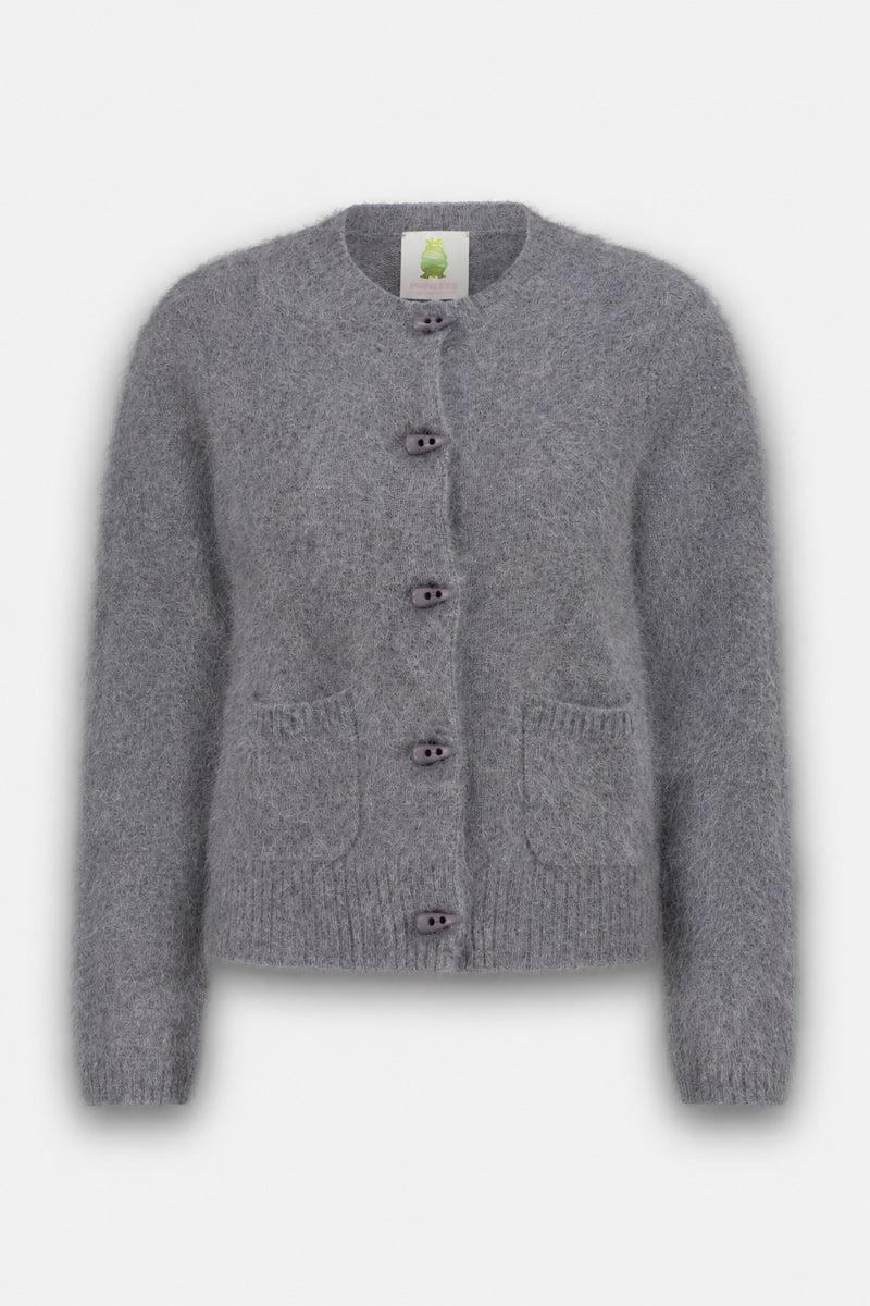 Eine flauschige Strickjacke mit langen Ärmeln in Grau, gefertigt aus gebürsteter Wolle. Sie verfügt über einen Rundhalsausschnitt, eine Knopfleiste mit fünf dunklen Knöpfen, zwei kleine Vordertaschen sowie gerippte Bündchen und einen gerippten Saum. Am Hals befindet sich ein Etikett mit einer grünen Frosch-Illustration. Die Rundhals-Strickjacke wird auf weißem Hintergrund präsentiert.