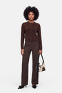 Eine Frau mit natürlichem Afro-Haar trägt eine braune Strickjacke aus gebürsteter Wolle, eine braune Nadelstreifenhose und schwarze Pumps mit spitzer Zehenpartie. In der Hand hält sie eine schwarz-weiße Handtasche mit Kuhmuster. Der Hintergrund ist schlicht weiß, was ihr stilvolles, aufeinander abgestimmtes Outfit und ihre selbstbewusste Haltung unterstreicht.