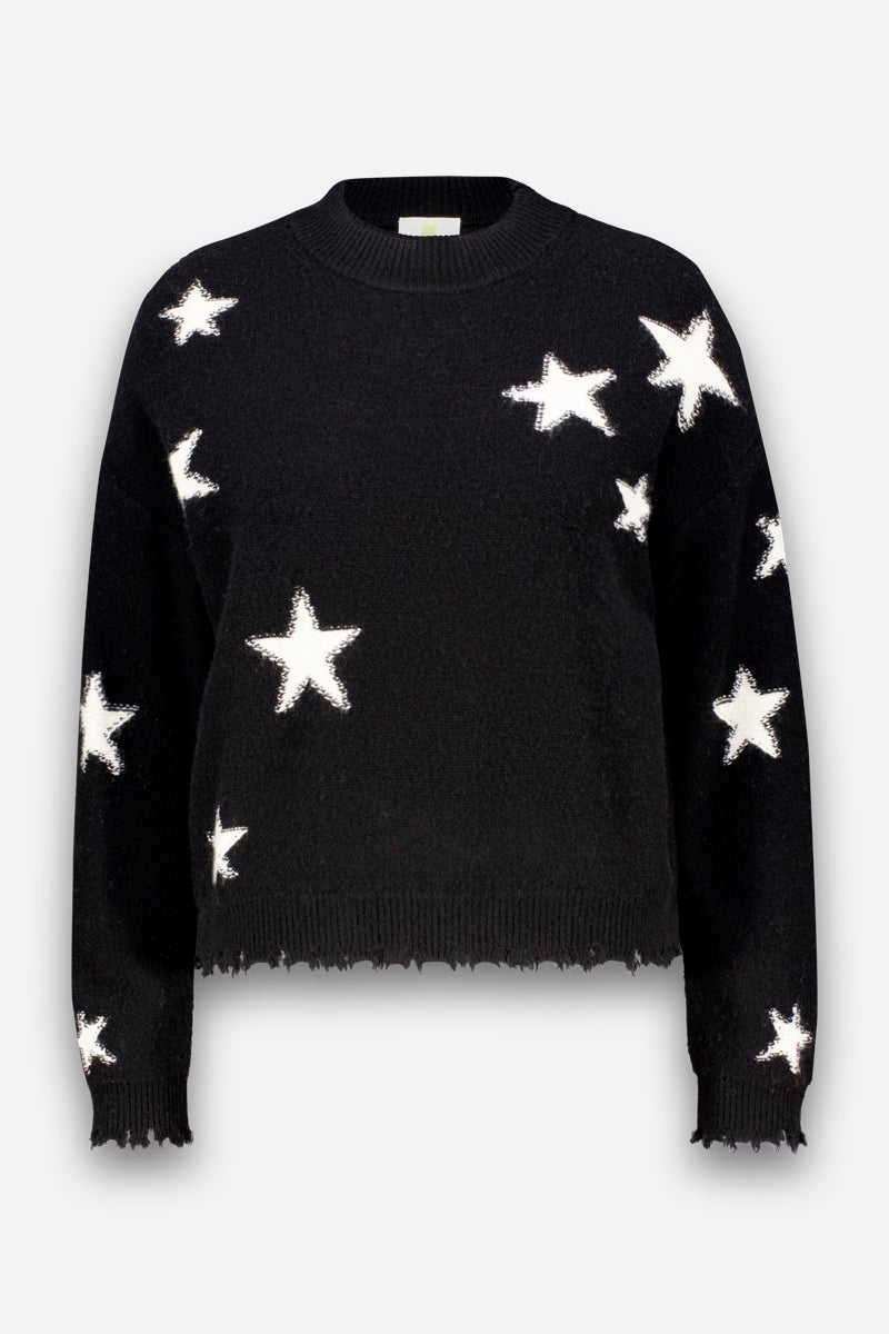 Ein schwarzer, langärmeliger Merino-Pullover mit Rundhalsausschnitt, der mit mehreren großen weißen Sternen im Sternen-Intarsia-Muster verziert ist, die über die Vorderseite, die Ärmel und die Schultern verteilt sind. Dieser Damenpullover ist mit gerippten Bündchen an Ärmeln, Saum und Halsausschnitt versehen und weist am Saum eine leicht abgenutzte, ausgefranste Kante auf.