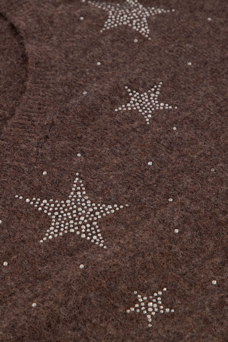 Nahaufnahme eines weichen, braunen Stoffes, möglicherweise eines Pullovers aus Alpaka-Wolle, mit mehreren Sternmotiven aus kleinen, weißen Strasssteinen, die in unterschiedlichen Größen und in unregelmäßigen Mustern angeordnet sind. Außerdem sind einige winzige Perlenpunkte über den Stoff verteilt.