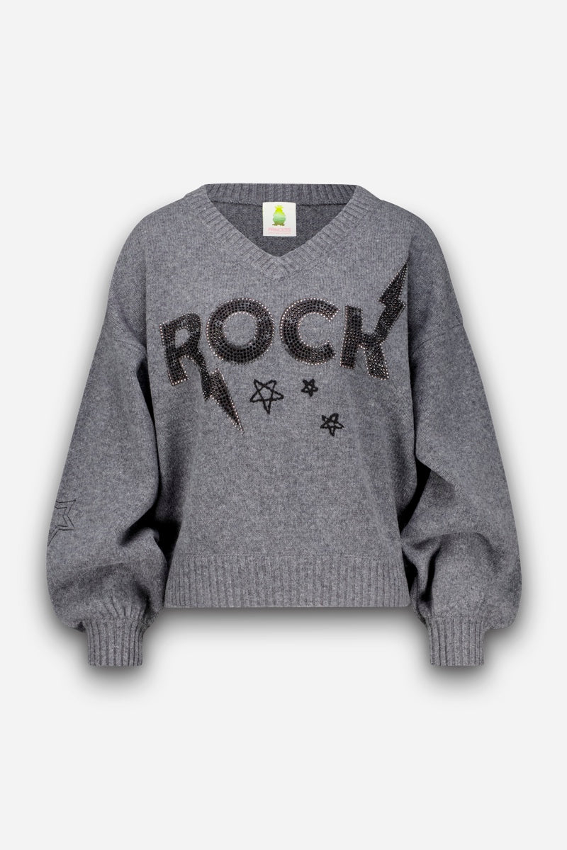 Grauer Pullover mit V-Ausschnitt, verziert mit dem Schriftzug „ROCK“ in großen schwarzen Buchstaben und Blitzen, die jeweils mit kleinen Metallnieten umrandet sind und so einen Hauch von Strassverzierung verleihen. Mit gerippten Bündchen und Saum, Ballonärmeln und kleinen schwarzen Sternmotiven. Dieser Pullover aus weicher Merinowolle wirkt kuschelig und leicht oversized. Einfarbiger, heller Hintergrund.