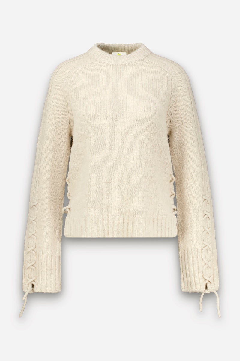Cremefarbener Strickpullover aus Alpaka-Wolle mit Rundhalsausschnitt, langen Raglanärmeln sowie gerippten Bündchen und Saum. Die Ärmel sind mit seitlichen Schnürdetails und gestrickten Bändern versehen, die dem ansonsten schlichten, kuscheligen Kleidungsstück eine dekorative Note verleihen. Der Pullover wird vor einem schlichten weißen Hintergrund präsentiert.