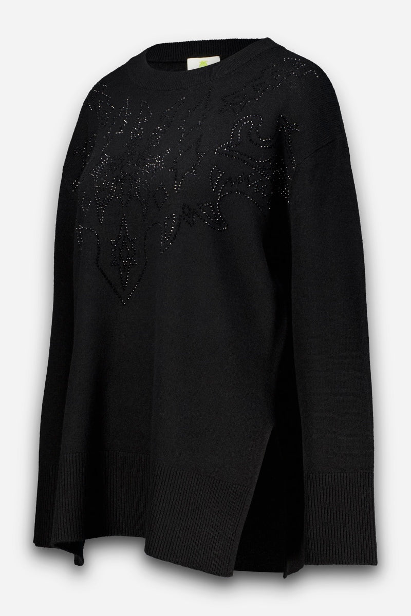 Schwarzer, übergroßer Pullover aus Merino-Kaschmir mit gerippten Bündchen und Saum, Seitenschlitz und einer dezenten, abstrakten Strassverzierung auf der Brust aus kleinen schwarzen Nieten oder Strasssteinen. Der Pullover hängt locker an einer unsichtbaren Schaufensterpuppe vor einem schlichten weißen Hintergrund.
