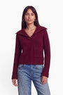 Eine Frau mit glattem, dunklem Haar trägt einen gerippten, weinroten Strickpullover mit V-Ausschnitt und weitem Kragen aus einer edlen Woll-Kaschmir-Mischung, dazu eine Brusttasche, kombiniert mit hellblauen Jeans. Sie steht entspannt frontal mit locker hängenden Armen, trägt eine Halskette mit Anhänger und Creolen-Ohrringe vor einem schlichten weißen Hintergrund.