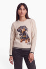 Eine Frau mit glattem braunem Haar trägt einen cremefarbenen Strickpullover für Damen mit einem realistischen Dackel-Motiv und kleinen schwarzen Herzen, dazu eine dunkle Jeans. Der gemütliche Pullover mit klassischem Rundhalsausschnitt hebt sich deutlich von ihrem neutralen Gesichtsausdruck ab, während sie vor einem weißen Hintergrund in die Kamera blickt.
