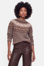 Eine Frau mit natürlich lockigem Haar trägt goldene Ohrringe und einen Strickpullover mit einem braunen Jacquard-Muster aus cremefarbenen und beigen geometrischen Motiven, gefertigt aus einer luxuriösen Woll-Kaschmir-Mischung. Dazu kombiniert sie eine braune Lederhose mit hoher Taille und steht selbstbewusst vor einem schlichten weißen Hintergrund.