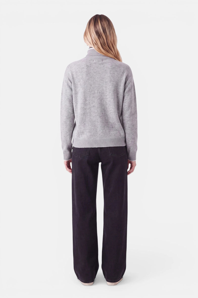 Eine Person, von hinten gesehen, die einen hellgrauen Rollkragenpullover aus einer Woll-Kaschmir-Mischung und eine dunkle Jeans trägt.