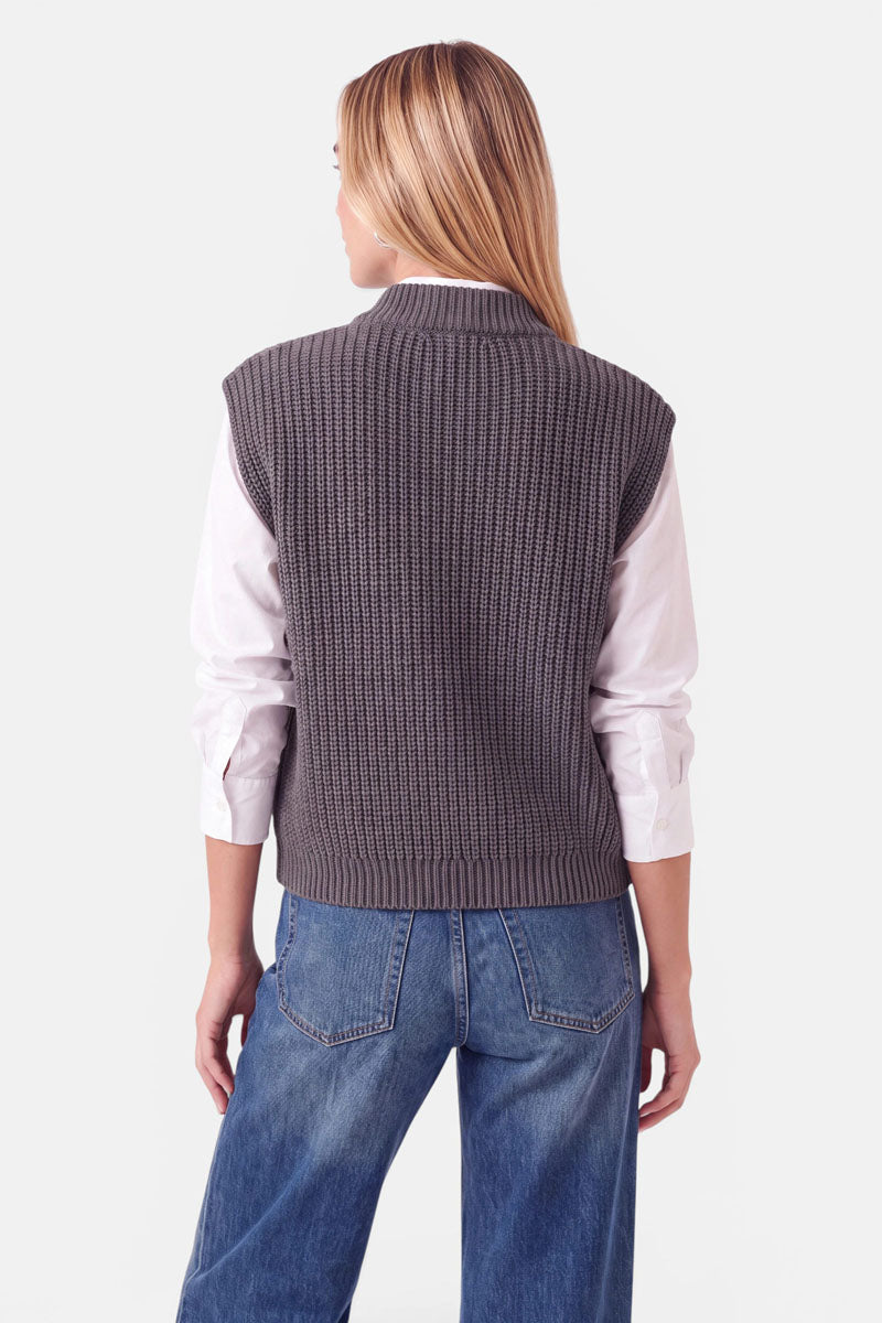 Eine Person, von hinten gesehen, die eine anthrazitgraue Strickweste aus Wolle und Kaschmir mit Stehkragen über einem weißen Hemd und einer blauen Jeans trägt.
