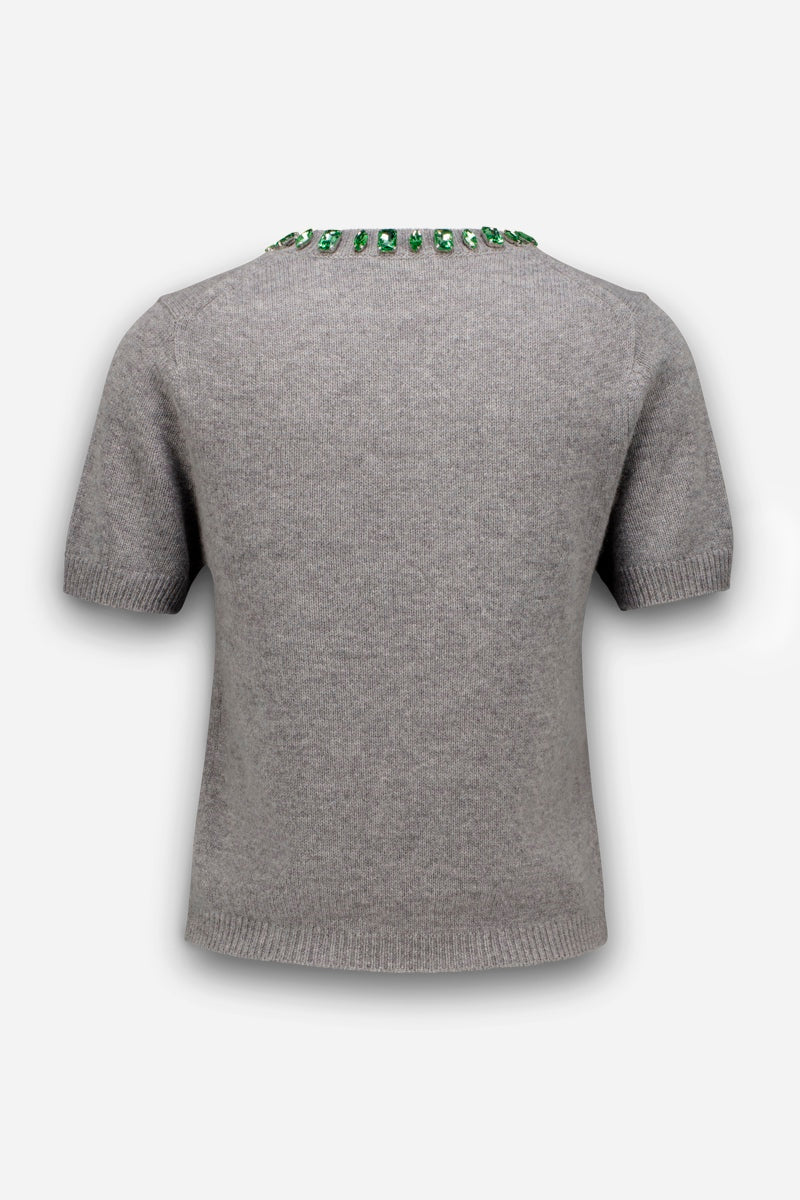 Ein grauer, kurzärmeliger Pullover aus einer Woll-Kaschmir-Mischung, von hinten gesehen, mit einem Rundhalsausschnitt, der durch eine Reihe funkelnder grüner Edelsteine verziert ist.