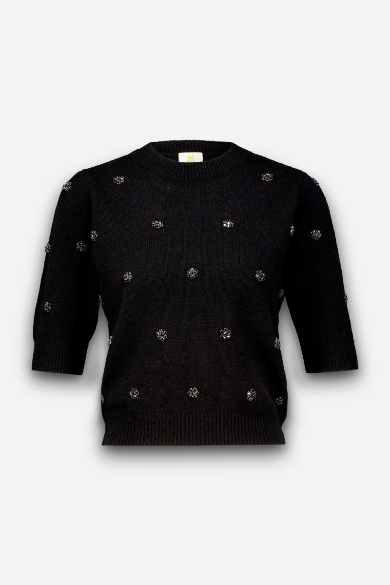 Ein schwarzer, kurzärmeliger Strickpullover mit geripptem Rundhalsausschnitt, gerippten Ärmelbündchen und geripptem Saum. Auf der Vorderseite und an den Ärmeln sind kleine, vereinzelte Blumenmotive aus Kristallen aufgebracht.