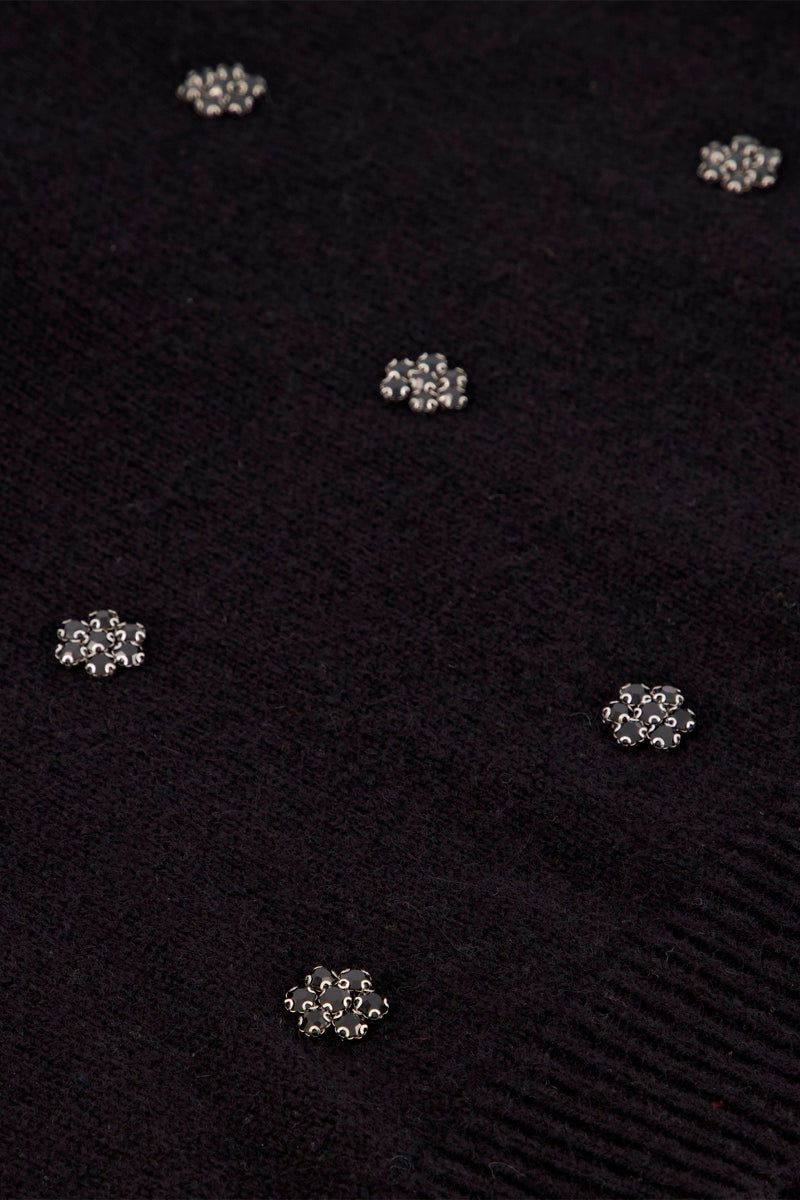 Ein schwarzer Strickpullover aus einer Woll-Alpaka-Mischung, verziert mit kleinen, silbernen, blumenförmigen Nieten, die über den Stoff verteilt sind.