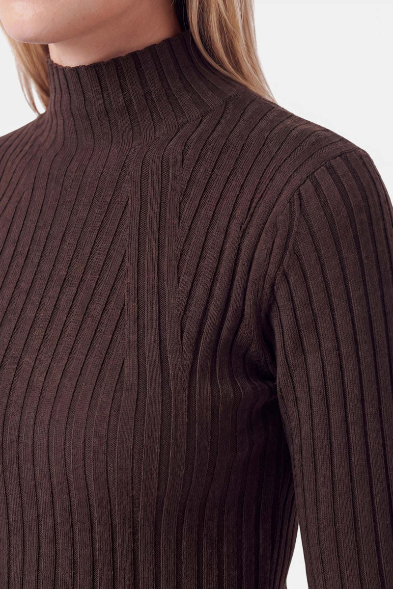 Eine Person trägt ein dunkelbraunes, geripptes Langarm-Oberteil mit Stehkragen. Das Kleidungsstück weist diagonale Rippendetails im Brustbereich und einen klassischen Stehkragen auf.