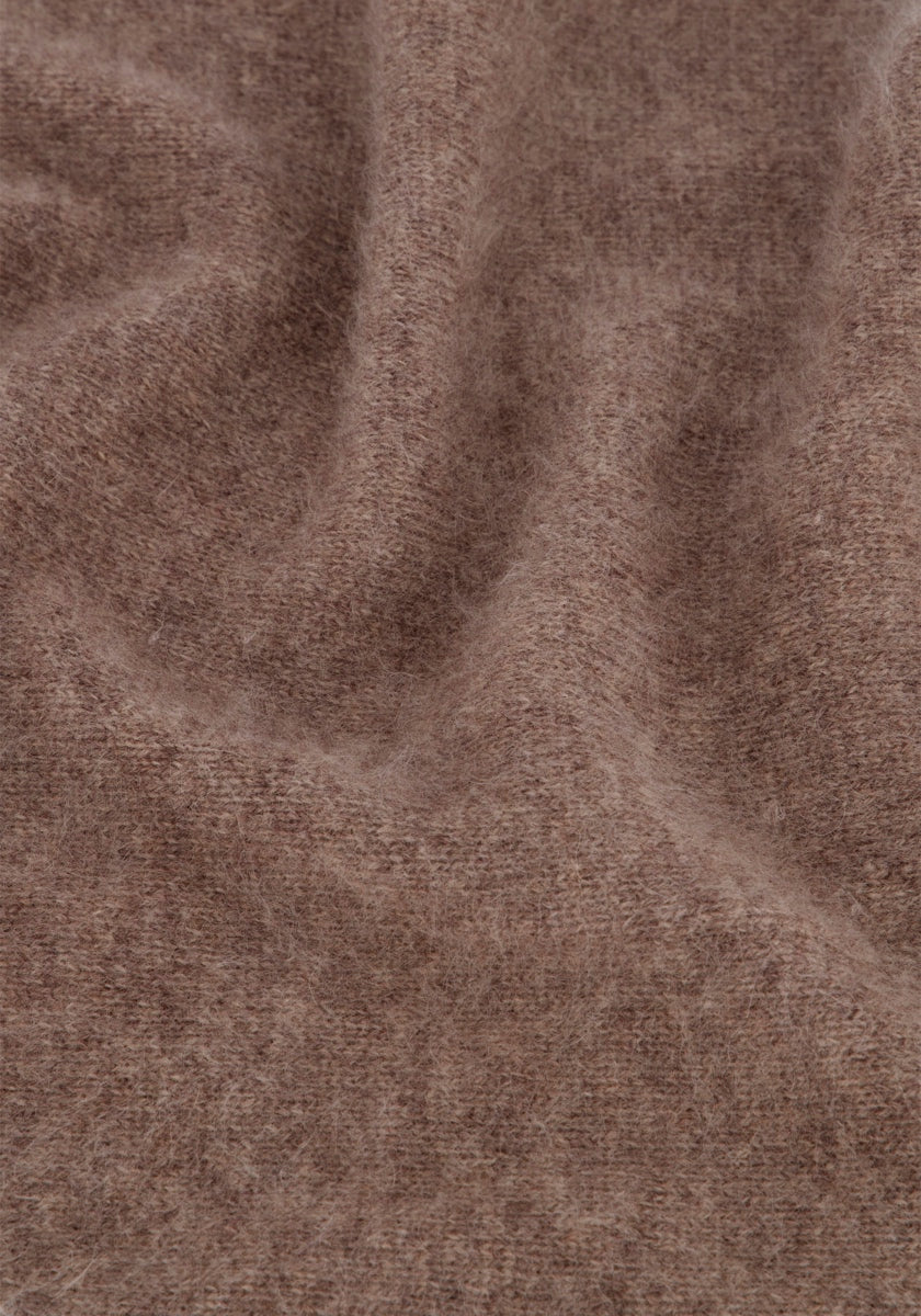 Eine Nahaufnahme von weichem, flauschigem braunem Stoff mit einer leicht unebenen Oberfläche, der an einen flauschigen Schal erinnert. Die Textur wirkt warm, mit sichtbaren Fasern aus gebürsteter Wolle und sanften, wellenförmigen Falten, die dezente Schatten und Lichtreflexe erzeugen.