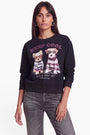 Eine Frau mit glattem braunem Haar trägt ein schwarzes Sweatshirt mit Hundemotiv, auf dem zwei illustrierte Hunde in Pullovern abgebildet sind, über denen der Schriftzug „KEEP COOL“ und darunter „HAVE A COSY DAY“ mit einer Prinzessin zu sehen ist. Das Sweatshirt ist aus weicher Baumwolle gefertigt und bietet höchsten Tragekomfort. Sein verspieltes Design wird durch dezente Strass-Details unterstrichen. Sie steht vor einem schlichten weißen Hintergrund und trägt eine graue Jeans.