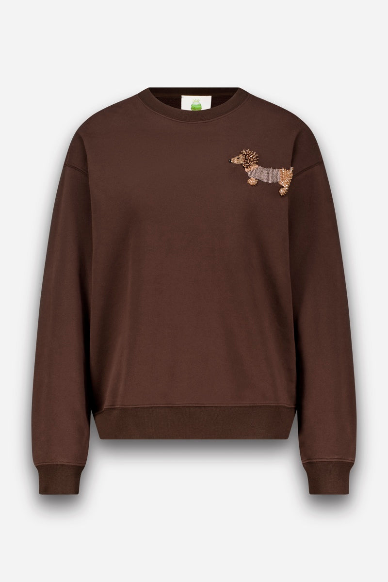 Ein braunes Sweatshirt mit Rundhalsausschnitt, gerippten Bündchen und Saum, gefertigt aus weicher Sweatshirt-Baumwolle. Auf der linken Brust befindet sich ein kleiner gestickter Dackel – eine bezaubernde Dackel-Applikation mit strukturiertem Körper und Schwanz. Der Hintergrund ist schlicht weiß, und das Sweatshirt wirkt ungetragen und ist ordentlich präsentiert.