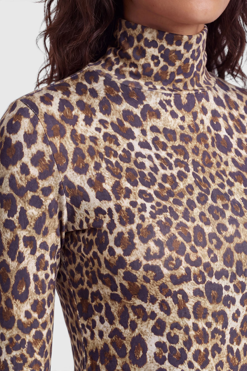 Eine Person trägt ein eng anliegendes Langarmshirt mit einem braunen, hellbraunen und schwarzen Leopardenmuster und einem stilvollen Stehkragen. Vor einem einfarbigen hellgrauen Hintergrund sind nur der Oberkörper und der Hals zu sehen. Das wellige Haar der Person ist teilweise zu sehen.