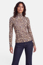 Eine Person mit welligem, dunklem Haar trägt ein eng anliegendes, langärmeliges Langarmshirt mit Leopardenmuster und Stehkragen sowie eine dunkle Jeans. Sie steht vor einem schlichten weißen Hintergrund, blickt mit neutralem Gesichtsausdruck und entspannter Körperhaltung nach vorne.