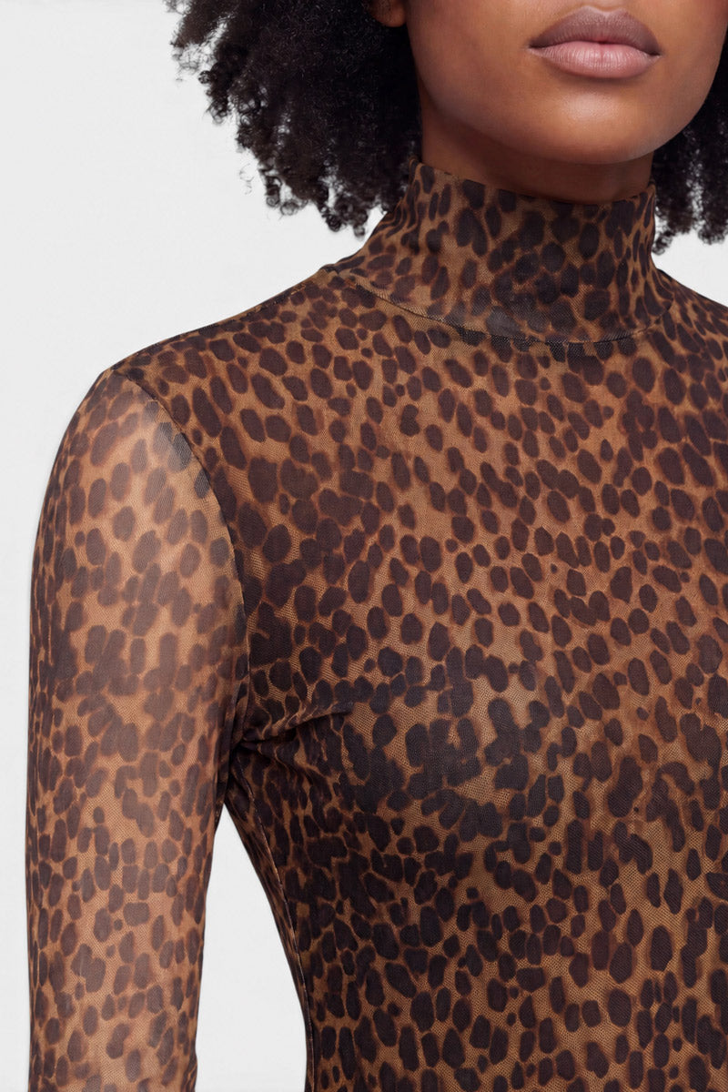 Eine Person mit mittelbrauner Haut und lockigem Haar trägt ein eng anliegendes, durchsichtiges Langarmshirt mit Leopardenmuster aus Mesh, das ein braun-schwarzes Leopardenmuster auf hellgrauem Hintergrund aufweist, das von der Gesichtsmitte bis zur Brust und am linken Arm zu sehen ist.