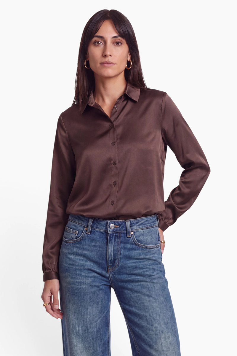 Eine Frau, die ein dunkelbraunes Stretch-Hemd mit Knöpfen trägt, das in eine blaue Jeans mit mittlerer Waschung gesteckt ist.