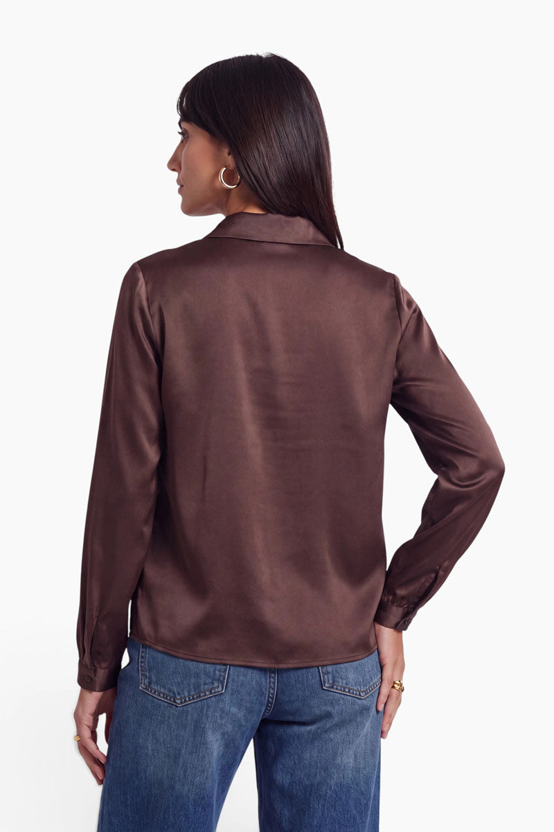 Eine Frau, von hinten gesehen, die ein braunes, elastisches Hemd mit Kragen und langen Ärmeln trägt, das in eine blaue Jeans gesteckt ist.