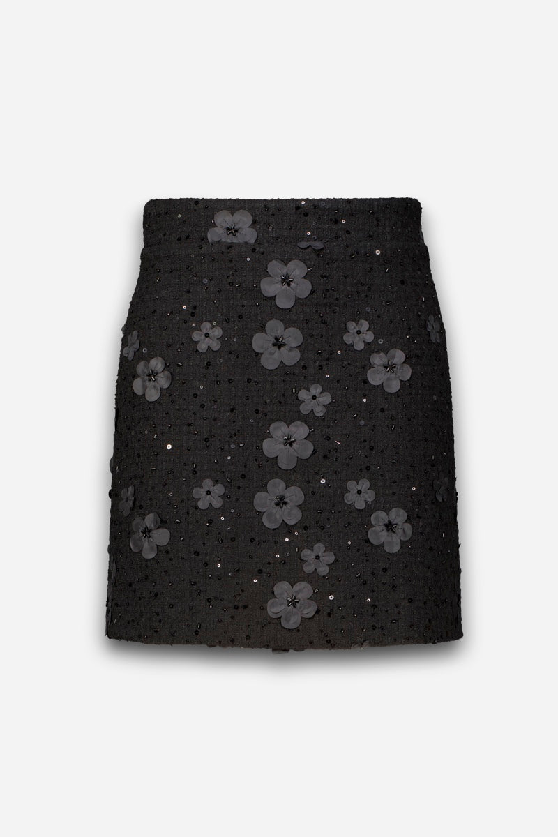 Ein schwarzer Minirock in Tweed-Optik, verziert mit vereinzelten Pailletten und dreidimensionalen Blumenapplikationen.