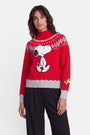Eine Frau mit welligem braunem Haar trägt einen roten Pullover im Norweger-Stil mit einem Snoopy-Aufdruck, der Snoopy und Woodstock zeigt, sowie grauen Mustern an Kragen, Ärmelbündchen und Saum. Sie steht mit dem Blick nach vorne vor einem schlichten weißen Hintergrund, trägt eine schwarze Hose und hat einen neutralen Gesichtsausdruck.