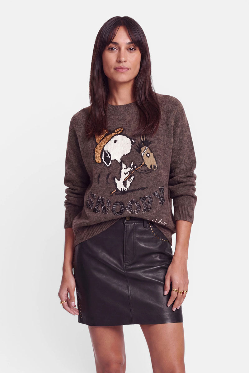 Eine Frau in einem braunen Pullover aus Alpaka-Wolle mit Snoopy-Intarsien und dezenten Strassverzierungen steht mit dem Blick nach vorne. Ihre Hände ruhen an den Seiten. Sie hat langes, glattes, dunkles Haar und einen neutralen Gesichtsausdruck. Der Hintergrund ist schlicht weiß.