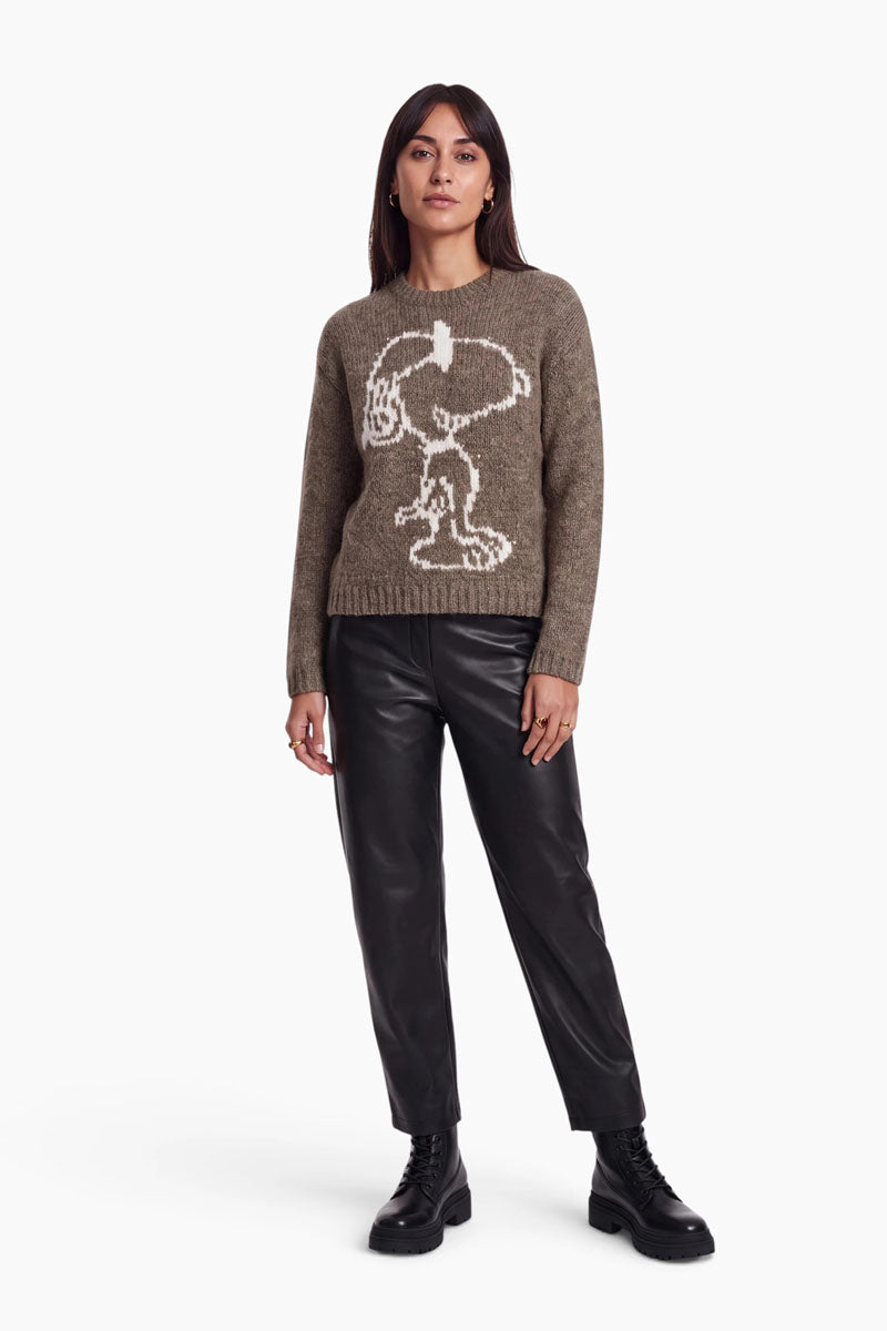 Eine Frau trägt einen braunen Pullover aus einer Mohair-Mischung mit Rundhalsausschnitt und einem großen weißen Snoopy-Intarsienmotiv. Dazu kombiniert sie den Pullover mit einer schwarzen Hose und schwarzen Schnürstiefeln.