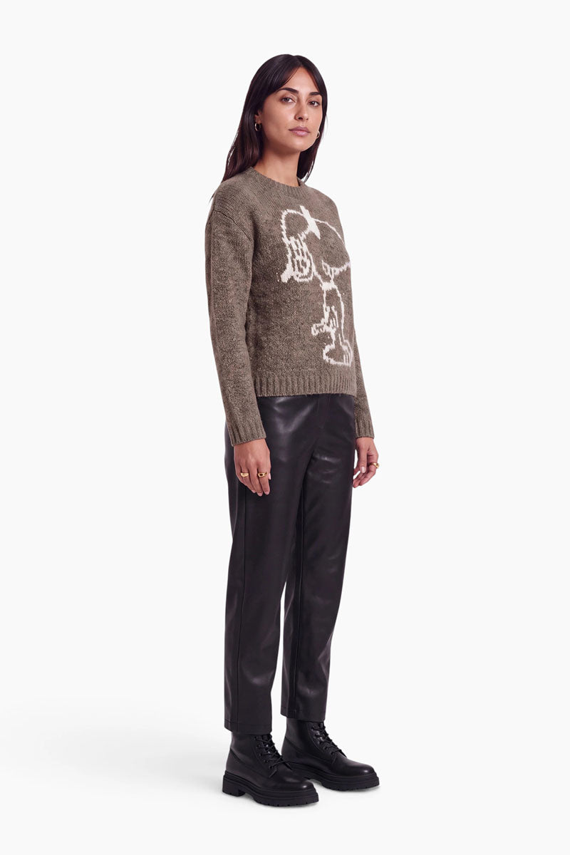 Eine Frau präsentiert einen braunen Pullover aus einer Mohair-Mischung mit einem großen weißen Snoopy-Intarsienmotiv, dazu trägt sie eine schwarze Hose und schwarze Schnürstiefel.